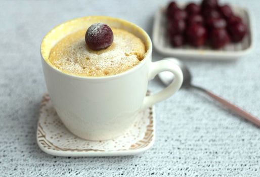 vanilla cupcake with cherries in a mug. Easy microwave cooking concept. The muffin is decorated with fresh cherries. White cup on a light background. Delicious sweet dessert. High quality photo