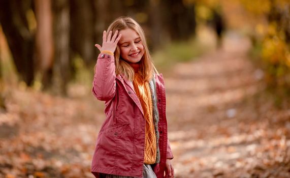 Beautiful girl kid looking at camera and smiling at nature with blurred yellow leaves on background. Cute child at park portrait