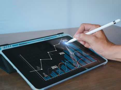 Hand of businessman use stylus pen point on tablet screen show analysis stock bar chart for target 2023. Analysts present a business plan with a graph showing the company's 2023 growth with a tablet.