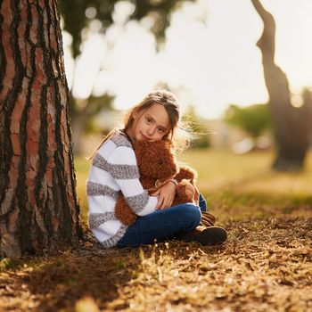 Portrait of a sweet little girl hugging her teddy bear while playing outside.