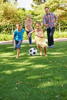 A happy family playing soccer in the park on a beautiful summer day.