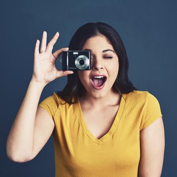 Studio portrait of an attractive young woman taking a photo against a blue background.