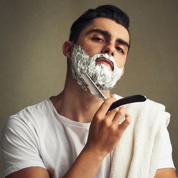 Cropped shot of a handsome young man shaving with a straight razor.