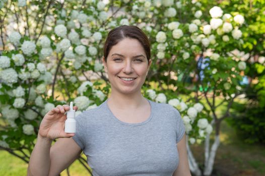 Happy woman demonstrating nasal spray on the background of a blossoming tree