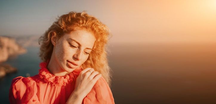 Side view a Young beautiful sensual woman in a red long dress posing on a volcanic rock high above the sea during sunset. Girl on the nature on overcast sky background. Fashion photo