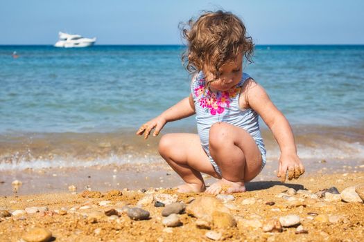 A little girl having fun playing with the sand on a beach in summer with the ocean horizon in the background