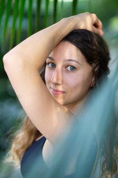 Young beautiful natural cheerful woman with healthy face and skin in exotic greenery. Closeup fresh face of attractive girl. Summer model. Natural beauty concept.