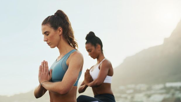 Cropped shot of two attractive young women sitting and meditating together on the beach during an overcast day.