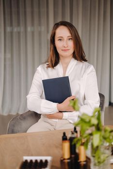 portrait of a smiling girl-woman sitting in an armchair. An aromatherapist in a white blouse is sitting in the office.