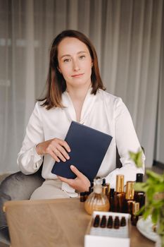 portrait of a smiling girl-woman sitting in an armchair. An aromatherapist in a white blouse is sitting in the office.