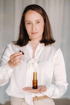 A woman in a white blouse holding a bottle of essential oil, aromatherapy.