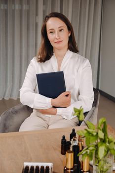 portrait of a smiling girl-woman sitting in an armchair. An aromatherapist in a white blouse is sitting in the office.