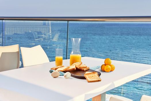 Table for two on outdoor hotel balcony with a sea view. European vacation breakfast, food selfie. Concept of a rest and healthy nutrition. There are toasts, eggs, orange juice.