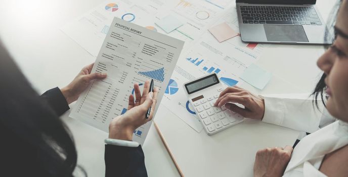 Top view of Finance business people or accountants point to the graph and use a calculator to calculate company income, expenses, taxes, and employee bonuses for Next year's improvement plan.