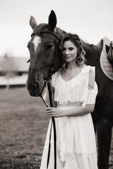 Beautiful girl in a white sundress next to a horse on an old ranch. black and white photo.