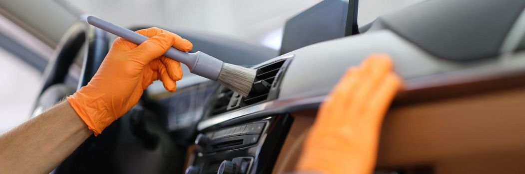 A man in a car wipes the dust with a brush, close-up. Detailing, cleaning of plastic surfaces inside the car, interior ozonation