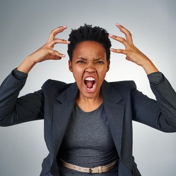 Portrait of an angry businesswoman yelling against a grey background.