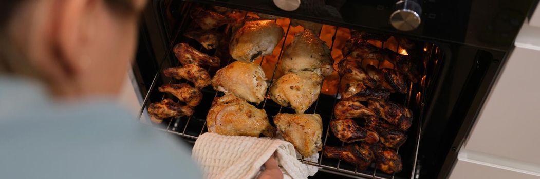 The woman determines the readiness of the chicken in the oven, close-up, blurry. BBQ cooking, grill wings