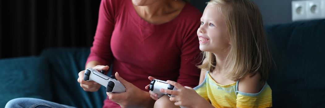 Mom and daughter are playing video games at home, close-up. Woman and child with game joysticks in hands