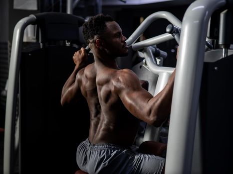 Shirtless african american man doing back exercises on a machine in the gym