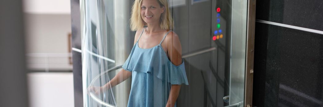 Happy woman in a fashionable dress rides in a transparent elevator, blurry. Glass passenger elevator in the building