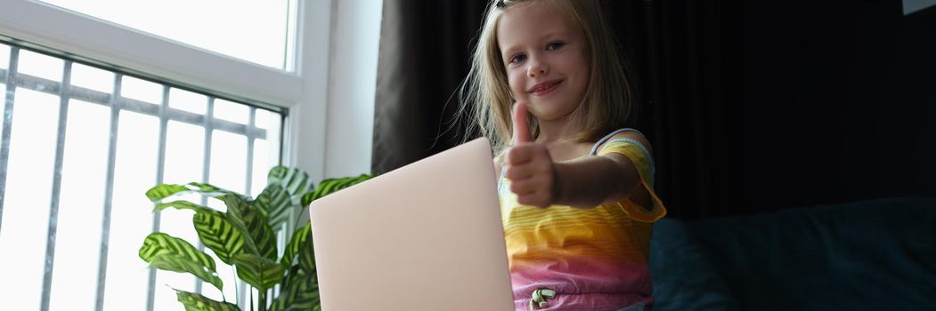 Little girl at home sitting on the couch holds a laptop, close-up. Computer literacy, children's cybersecurity