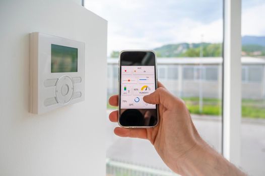 Hand holding a mobile phone showing an home automation app to manage online technology in a modern loft.