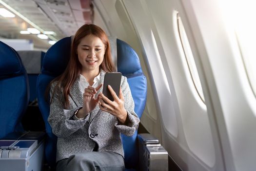 Travel and technology. Young woman in plane using smartphone while sitting in airplane seat.