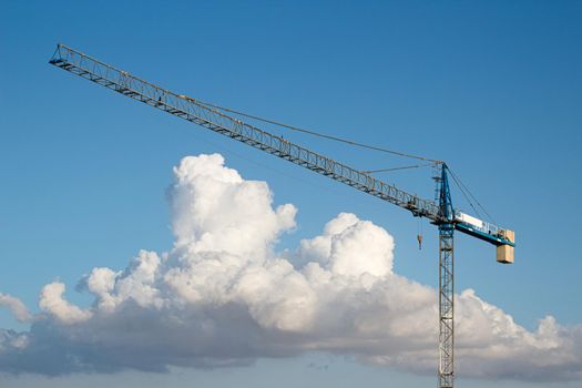 Industrial construction tower crane against a blue sky background with dramatic clouds