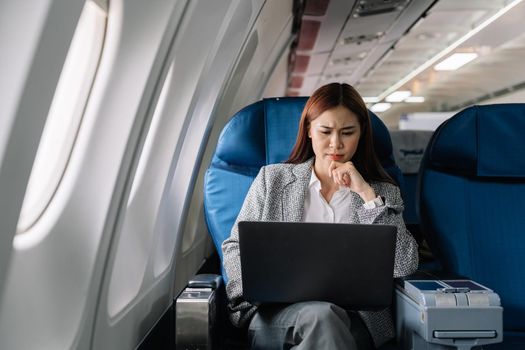 serious asian young woman using laptop sitting near windows at first class on airplane during flight, Traveling and Business concept.