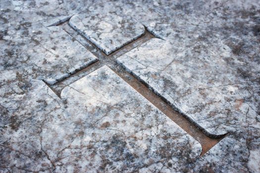 Christian cross emblem engraved in marble tombstone in a graveyard