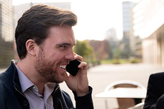 smiling businessman talking by phone sitting on a terrace in the financial district, concept of entrepreneurship and business, copy space for text