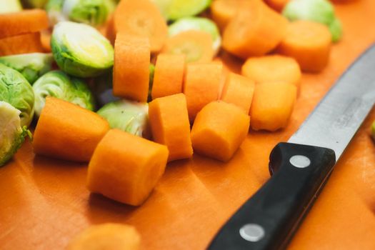 Sliced carrots and halved brussel sprouts on a vegetable chopping board with a sharp knife