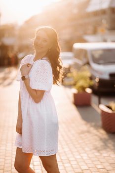 A beautiful woman in a white dress at sunset in the city. Evening street photography.