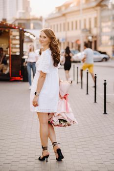 A happy woman in a white dress at sunset with a bouquet of flowers in the city.