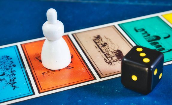 Close-up of board game squares with player piece and black die with yellow dots