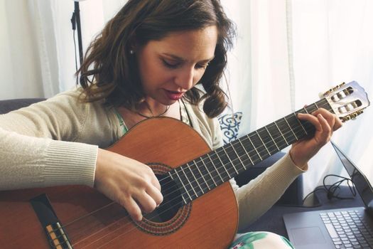 Attractive young lady playing and recording music using a Spanish classical guitar and a laptop