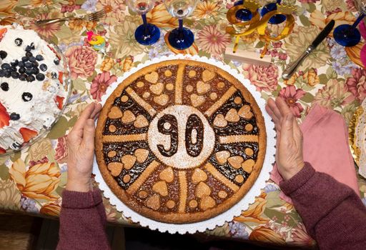 Senior woman holds her 90's birthday cake on the table