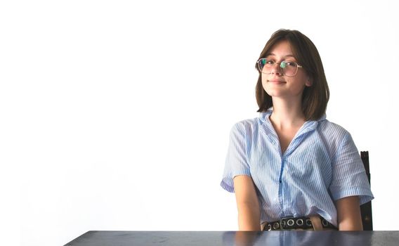 Young pretty female student wearing glasses and sitting at a desk against a pure white background