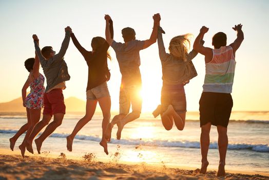 Rearview shot of a group of young friends jumping into the air while holding hands at the beach.