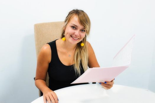 Attractive blonde Scandinavian woman sitting at an office desk smiling and holding a folder