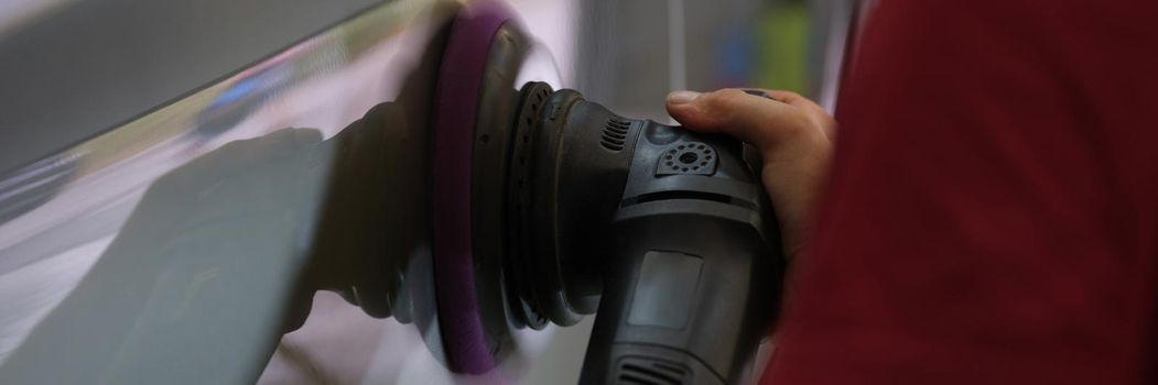 A repairman polishes a car body, close-up of a hand. Equipment for removing scratches, removing paint irregularities