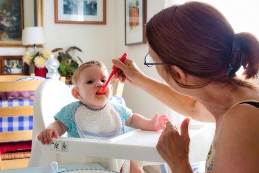 Little child being fed by her grandmother in a plastic high-chair