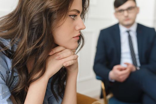 A young woman at a psychiatrist's or psychologist's appointment is worried, holds her hands to her face and tries to talk about her problems