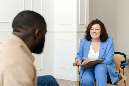 A female psychologist conducts psychological therapy with an African American man, makes notes in a clipboard