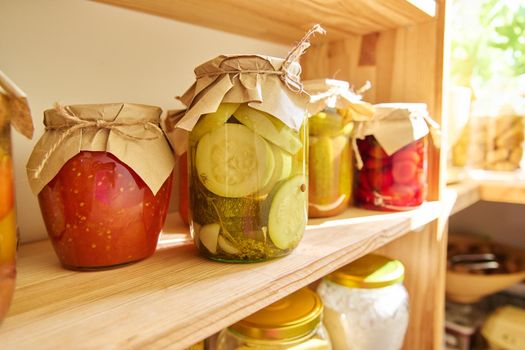 Storage of food in kitchen in pantry. Pickled canned vegetables and fruits on shelf, jar of marinated zucchini and tomato sauce close-up. Cooking at home, homemade preservation, household