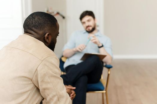 Unhappy young black man having session with professional psychologist at mental health clinic. Professional psychological help concept