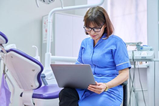 Doctor nurse dentist sitting in the office using a laptop. Dentistry, health care, treatment, work, profession, medicine concept