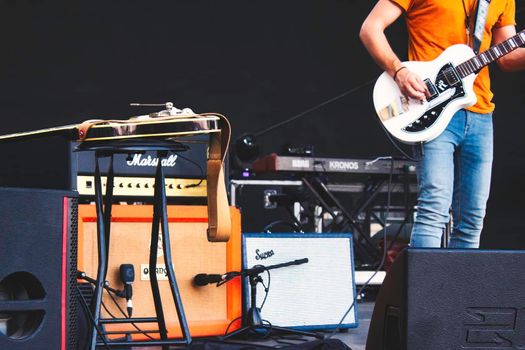 A guitarist on stage surrounded by musical equipment and electric guitar amplifiers