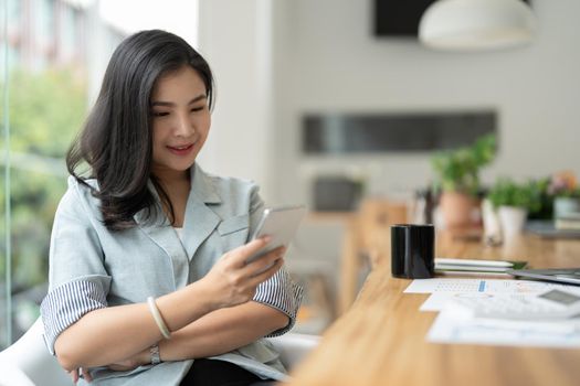 Smiling asian businesswoman using phone in office. Small business entrepreneur looking at her mobile phone and smiling
